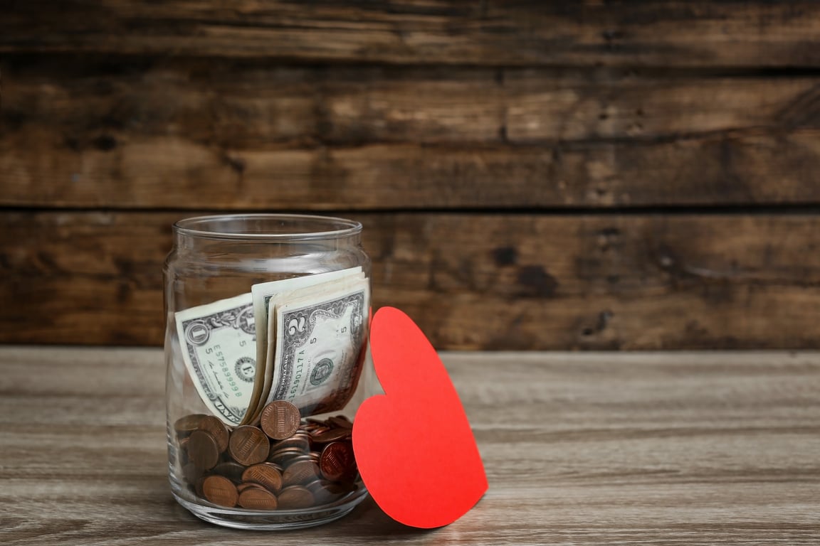 Donation Jar with Money and Red Heart on Table. Space for Text